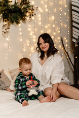 Mother and son are sitting in the bedroom on the bed in pajamas and the baby is drinking milk