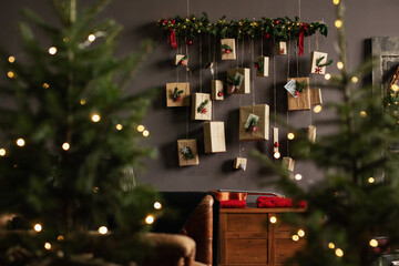 Advent calendar of kraft paper gifts hanging from a lit garland on a dark wall with blurred...