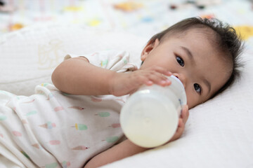 Obraz premium Adorable baby girl drinking milk from bottle lying on bed