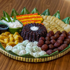 Assorted traditional Indonesian snacks and desserts known as kue basah, beautifully arranged on a bamboo tray lined with banana leaves. Includes klepon, lupis, black sticky rice and getuk