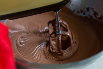 Electric mixer whipping chocolate cream in bowl for dessert preparation
