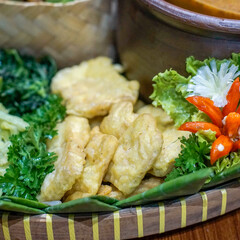Close-up of traditional Indonesian Tempe Mendoan, thin battered and crispy fried tempe served on a banana leaf with chili garnish. High texture detail, ideal for food blogs, menus and culinary editor