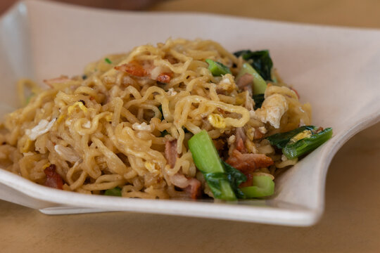 Close-up of traditional Tuaran Mee, a famous Sabah specialty, featuring golden, wok-fried noodles topped with slices of char siu, vegetables, and egg.