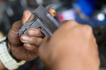 Close-up of a mechanic's hands using a vernier caliper to take a precise measurement of a small component during technical inspection or engineering work.
