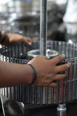 Worker's hands aligning a large, complex metal gear drum assembly onto a threaded shaft during maintenance or overhaul of heavy industrial machinery.