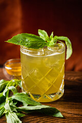 A glass of herbal drink with fresh basil and honey sits on the table