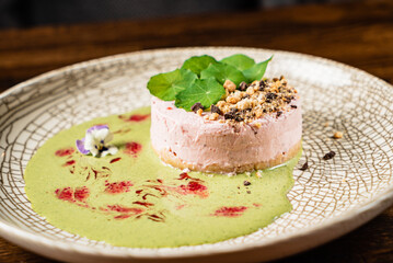 A beautiful dessert featuring layers of berry mousse with green sauce, nuts, and flower garnish