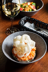 Savor the elegance of fish tartare topped with parmesan foam, accompanied by a glass of wine