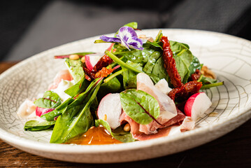 Colorful salad features spinach, radishes, and sun-dried tomatoes garnished with an edible flower