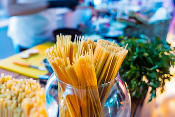Pasta stands tall in a glass container as friends gather to cook a delightful meal together