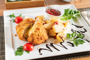 A plate features golden fried chicken alongside seasoned potatoes and fresh cherry tomatoes
