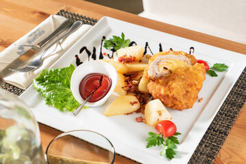 Crispy chicken stuffed with cheese paired with potatoes, lettuce, and flavorful sauce on a table