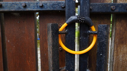 Yellow combination padlock with numeric code attached to a wooden and iron gate, partially blurred. Security concept with selective focus, perfect for background, design, or safety-related themes