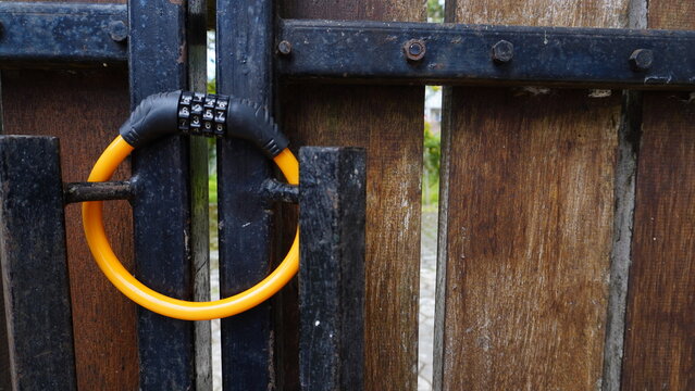 Yellow combination padlock with numeric code attached to a wooden and iron gate, partially blurred. Security concept with selective focus, perfect for background, design, or safety-related themes