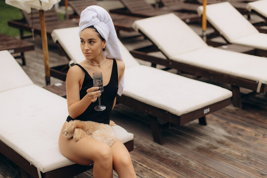Young woman relaxing with her dog at poolside resort, enjoying a glass of wine - Powered by Adobe