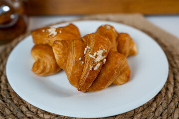 Close-up of golden baked croissants on white plate. Cozy homemade breakfast with warm daylight.