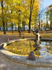 Saint Petersburg. View of bronze fountain Boy with Horn (1887) in Nikolsky Garden near Nikolay-Bogoyavlensky Naval Cathedral on autumn sunny day with yellow fallen leaves