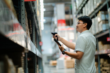 A man is standing in a warehouse, holding a tablet and a gun. He is looking at the tablet, which is...