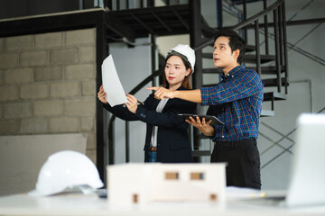 Asian architects discussing blueprints and house models during a site meeting. Indoor construction planning and teamwork concept.