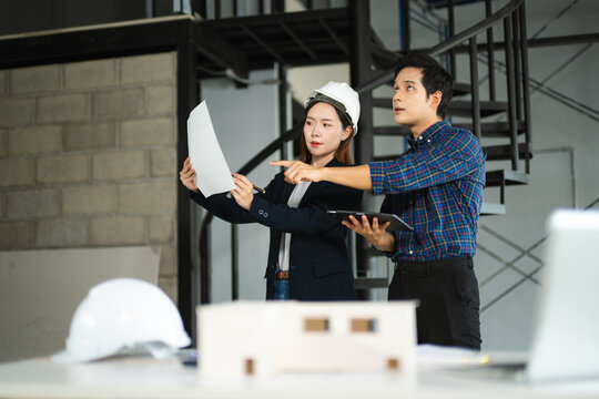 Asian architects discussing blueprints and house models during a site meeting. Indoor construction planning and teamwork concept.