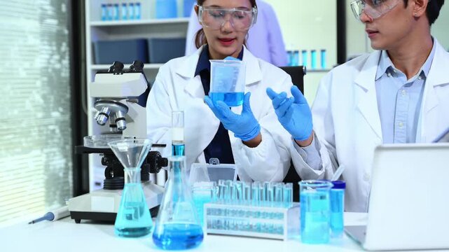 Closeup of Asian scientists using pipette and blue liquids in a modern lab, showcasing biotechnology, chemistry, and scientific innovation.