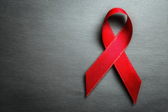 A vivid red awareness ribbon rests on a dark, textured surface, symbolizing support and solidarity. This striking image offers excellent copy space, ideal for health advocacy, fundraising, or educatio