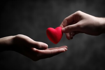 A visually striking close-up features two human hands engaged in a tender exchange, with one hand gently offering a plush, vibrant red heart to another awaiting palm. The composition is set against a 