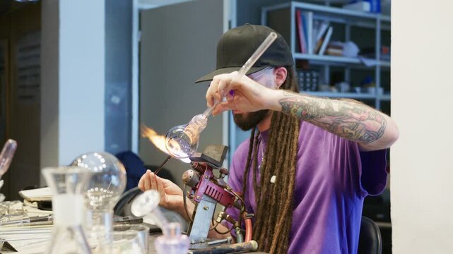 A young rastafari artisan demonstrates his talent by skillfully crafting a glass piece, using intricate techniques and special tools. The lively workshop reflects creativity and passion.