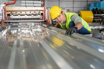 Worker inspecting a newly produced metal sheet roofing panel on the assembly line of a heavy industrial roll forming machine in the factory.