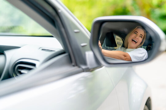Happy woman enjoying a road trip while looking out the car window on a sunny day - Powered by Adobe