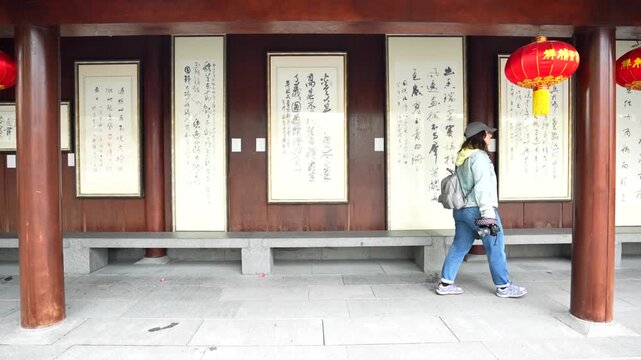 Caucasian tourist woman with a camera walks along a corridor with Chinese proverbs and red lanterns at Longhua Temple, Shanghai, China