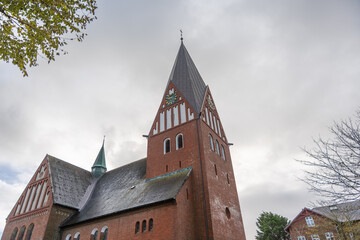 Historic red brick church with tall spire and clock under cloudy sky. Traditional northern European architecture in daylight.