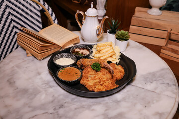 A mouth-watering image of fried chicken and a diverse meal. Beside the plate are a teapot, a book and decoration