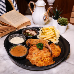 A delicious plate of meal, including pork chop, fried food and dip sauce on the table, which looks appetizing