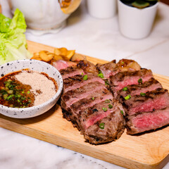 Sliced grilled steak on a wooden board served with sauce, evoking a sense of culinary delight and satisfaction. This scene presents a perfectly cooked steak, offering a visual feast