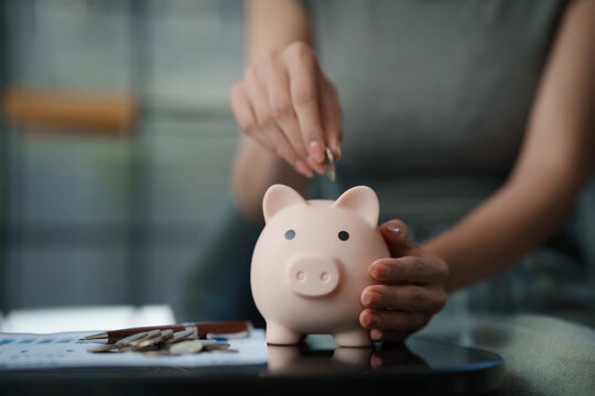 Woman writing financial plans in a notebook beside a piggy bank and coins on a table, symbolizing budgeting and savings management. - Powered by Adobe