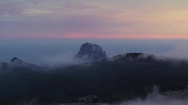 Aerial footage of mystical island of Es Vedra in Ibiza, Spain. Rocky peak emerges from a sea of clouds at sunset with Mediterranean Sea background