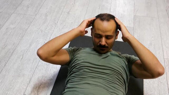 Man with mustache doing sit-ups on the floor in a gym. Athlete in a green t-shirt and shorts doing core training. 4K.