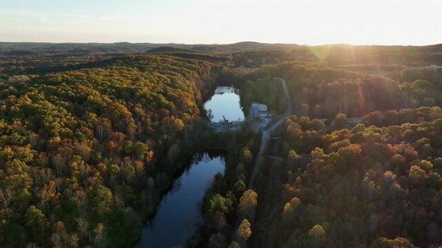 Aerial wide shot of tranquil river between dense colored forest trees during golden sunset. Peaceful atmosphere in fall season. Virginia, USA.