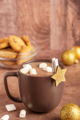 Cozy hot chocolate drink or homemade cocoa decorated with marshmallows served in ceramics cup on brown table with festive christmas golden star decor, shiny baubles and sweet cookies as party dessert