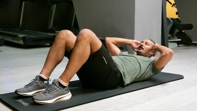 Man with mustache in a green t-shirt doing sit-ups on the floor. 4K footage of an athlete in his 30s performing a core workout in the gym.