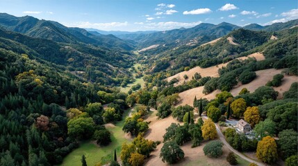 Fototapeta premium Panoramic View of Rolling Green Hills Covered in Autumn Trees with a Small White Building Nestled in the Landscape Under a Blue Sky