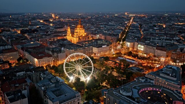 Twilight over Budapest&rsquo;s heart, where St. Stephen&rsquo;s Basilica and the glowing Budapest Eye shine amid elegant streets and historic charm.