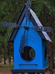 A birdhouse is an artificial nesting place for birds.
The birdhouse has four blades, similar to a propeller.
He is hanging on a tree.
The birdhouse is located in the park.