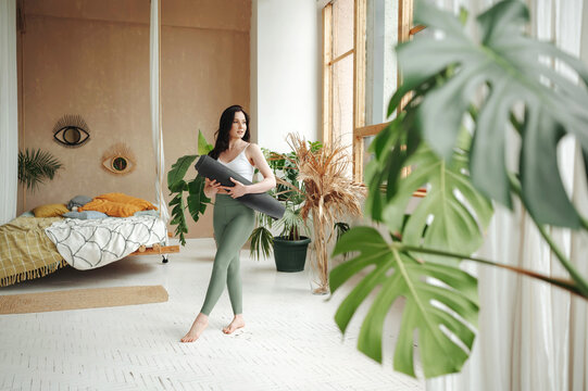 Female standing with crossed legs and holding yoga mat