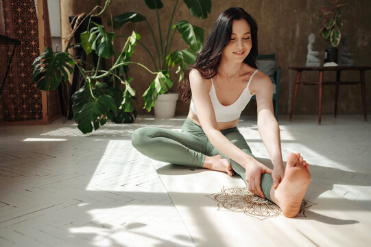 Active trainee making exercises and stretching leg indoors