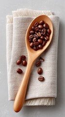 Wooden spoon filled with roasted coffee beans rests on textured fabric with scattered beans on a light grey surface studio lighting