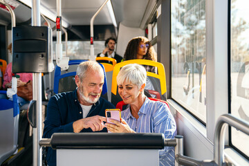 Senior couple traveling on a public city bus, happily sharing and interacting with a smartphone screen together