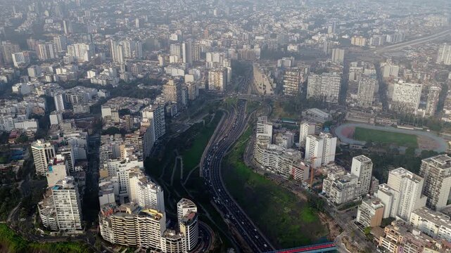 High altitude aerial view of Miraflores, Lima, focusing on Bajada Balta highway cutting through a green valley amid modern buildings