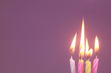 Fototapeta premium Several different birthday cake candles burning on purple background. Copy space for text.